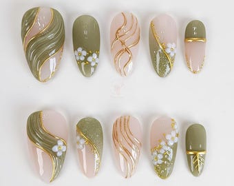 May include: A set of ten artificial nails in various designs. The nails feature a combination of olive green, pale pink, and gold accents. Some nails have floral details, while others showcase abstract gold lines and swirls.