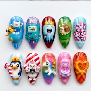 Peut inclure: Dix modèles de nail art colorés et fantaisistes. Chaque ongle présente un personnage de dessin animé ou un motif différent, comme un pingouin, un bonhomme de neige, une licorne et des personnages d'Adventure Time. Les ongles sont peints dans diverses couleurs et textures.