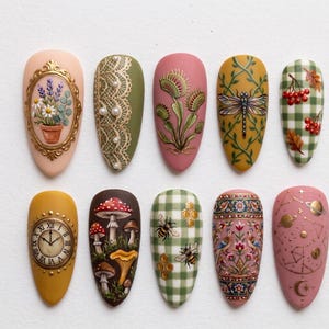 May include: Ten almond-shaped nail designs are displayed. The designs feature a gold framed floral arrangement, lace, a Venus flytrap, a dragonfly, a plaid pattern with berries, a clock, mushrooms, bees, birds, and a celestial theme.