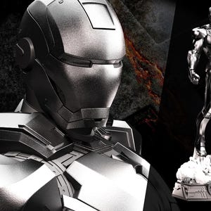 May include: A detailed, grayscale image featuring a metallic Iron Man suit and a War Machine helmet. The text "AVENGERS ASSEMBLE" is in the upper left corner. A full Iron Man figure stands on a base in the background.