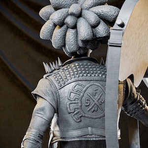 May include: A gray sculpture of a figure with a textured headpiece and a studded leather jacket. The jacket features a circular emblem on the back. The figure is holding a large, gray axe with a strap.