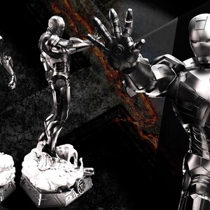 May include: A metallic silver Iron Man statue in a dynamic pose, with the text "AVENGERS ASSEMBLE" in the upper left corner. The statue is on a white base, and the background is dark with a fiery effect.