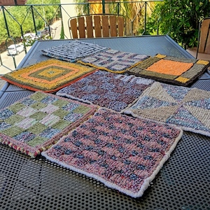 Könnte beinhalten: Eine Sammlung handgefertigter, quadratischer Untersetzer oder Topflappen. Jeder Untersetzer hat ein einzigartiges Muster und Farbschema, darunter Schachbrett- und geometrische Designs. Die Untersetzer bestehen aus einem strukturierten, gewebten Material.