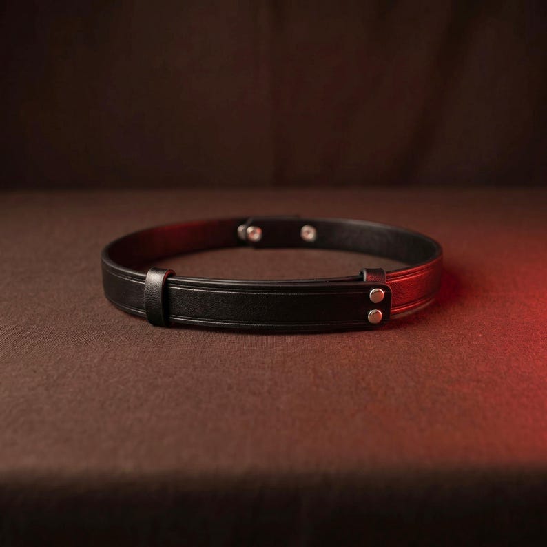 May include: A black leather belt featuring a smooth, minimalist design with a single leather keeper loop. The belt is secured with two silver-toned metal rivets on the strap, providing a clean, functional aesthetic for this adjustable accessory.