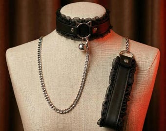 May include: Black leather choker with a cat-shaped ring and a silver bell pendant. The choker has a delicate black lace trim. A silver chain and a matching black leather wrist cuff with lace trim complete the set.