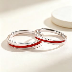 May include: Two silver-toned rings featuring a smooth, polished finish and a single, continuous inlay of vibrant red enamel that wraps around the centre of each band. The rings have an open-ended design, allowing for adjustable sizing for a comfortable fit.