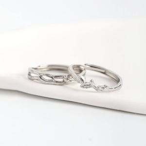 May include: Two silver rings with nature-inspired designs. One ring features a textured branch pattern, while the other has a delicate leaf motif. The rings are set against a white background, highlighting their intricate details.