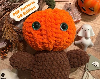 Pode incluir: Uma abóbora laranja de pelúcia com olhos grandes com bordas verdes e um caule verde está sentada em um corpo marrom com os braços estendidos. A imagem inclui elementos decorativos de Halloween, como estatuetas de fantasmas e uma faixa. O texto na imagem diz "PDF Pattern: US Edition."