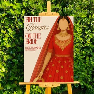 May include: A decorative sign on a wooden easel with the text "Pin the Bangles on the Bride." The illustration features a woman in a red dress and veil. The game instructions are below the title.
