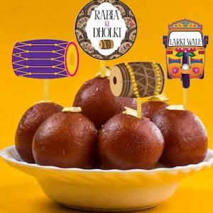 Può includere: Una ciotola gialla piena di dessert rotondi e marroni, gulab jamun. I topper decorativi includono un tamburo, un tuk-tuk e un design circolare con il testo "RABIA KI DHOLKI". Lo sfondo è giallo pieno.