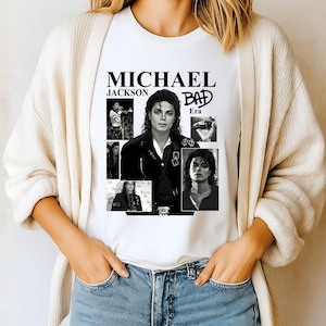 May include: White t-shirt featuring a collage of black and white images of Michael Jackson. The shirt includes the text "MICHAEL JACKSON" above the word "BAD" and the word "Era".