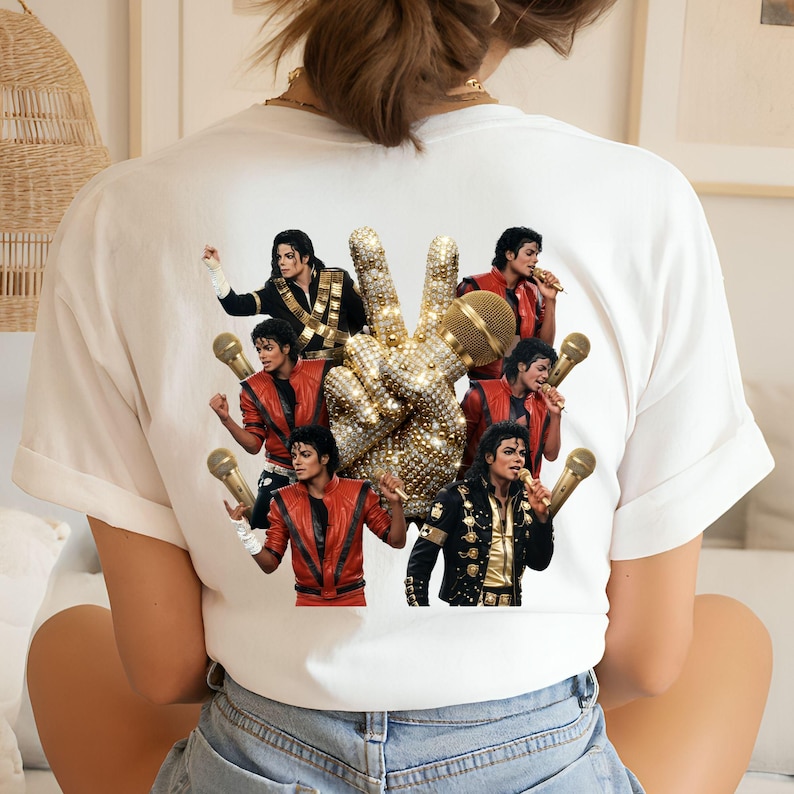May include: White t-shirt featuring a graphic of Michael Jackson in various poses, with a bedazzled peace sign and microphones. The design includes images of Jackson in a red jacket, black jacket, and gold microphone.