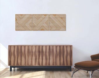 May include: Three square wooden wall panels featuring a light brown finish and a geometric pattern of raised parallel lines arranged in various diagonal directions, mounted horizontally in a row above a wooden sideboard cabinet.