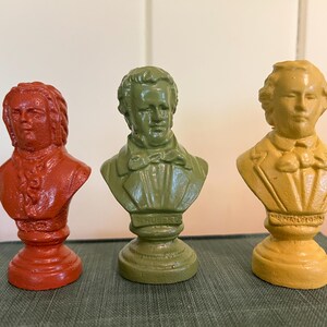 May include: Three colorful busts of historical figures. The busts are painted in shades of red, green, and yellow. Each bust is mounted on a pedestal. The busts are arranged in a row, with the red bust on the left, the green bust in the middle, and the yellow bust on the right.