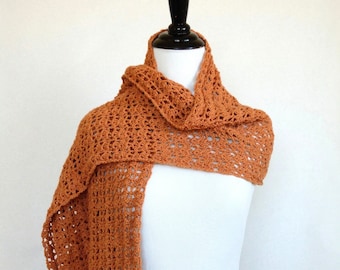 May include: A terracotta-coloured, open-weave scarf draped over a white mannequin. The scarf is made of a soft, textured material and features a delicate, lacy pattern. The scarf is displayed on a black stand against a white background.