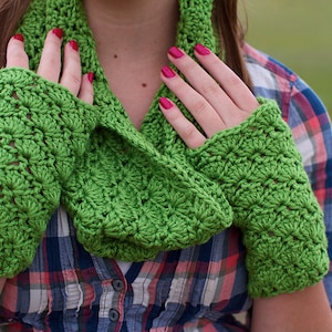 May include: A vibrant green crochet scarf and fingerless gloves set. The handmade set has a textured, openwork design. The gloves cover the hand up to the knuckles. The scarf is around the neck. The background is a plaid shirt.