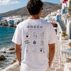 Może przedstawiać: Biały t-shirt z krótkim rękawem z napisem GREEK STARTER PACK oraz siatką dziewięciu czarnych ikon liniowych przedstawiających napój kawowy, różaniec, plastikowe krzesło, grę w tryktraka, niebieski amulet oka, ikonę religijną, butelkę piwa, kawałek arbuza oraz głośnik z klarnetem.