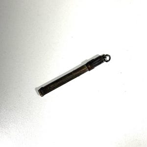 Könnte beinhalten: Ein kleiner Bleistifthalter aus Metall im antiken Stil mit dunkler, gealterter Oberfläche. Der Bleistifthalter ist rechteckig mit einem Ring oben zur Befestigung. Das Metall hat ein strukturiertes Aussehen, was darauf hindeutet, dass es vintage ist oder gut benutzt wurde.