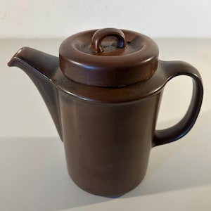 Op de afbeelding: Een bruine keramische theepot met bijpassende deksel en handvat. De theepot heeft een tuit om uit te schenken en een afgeronde body. Het deksel heeft een klein handvat voor gemakkelijk verwijderen. De theepot is effen donkerbruin.