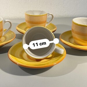 Può includere: Un set di quattro tazzine da caffè espresso e piattini in ceramica. Le tazze e i piattini sono gialli con strisce arancioni. La tazza è larga 11 cm. L'interno della tazza è bianco.