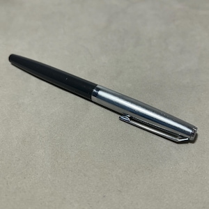 May include: A sleek writing pen featuring a matte black barrel and a polished silver cap. The cap includes a slender, integrated metal pocket clip. The design is clean and functional, showcasing a two-tone aesthetic with a smooth transition between the black body and the metallic silver cap section.