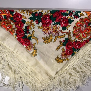 Könnte beinhalten: Cremefarbener Schal mit einem Blumenmuster mit roten Rosen, grünen Blättern und gelben Akzenten. Der Schal hat einen Fransenrand und ein detailliertes, farbenfrohes Design. Das Blumenmuster konzentriert sich in der Mitte und in den Ecken.