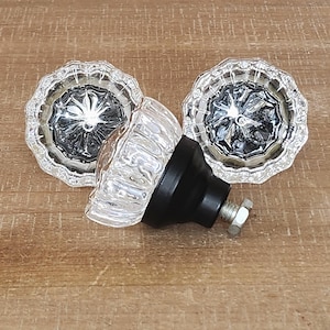 Puede incluir: Tres pomos de puerta de cristal transparente con base de metal negro y tornillo plateado. Los pomos tienen un diseño facetado y un centro elevado.