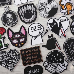 Puede incluir: Una colección de parches bordados con varios diseños. Incluye una calavera en una botella, un gato con múltiples ojos, un corazón con la palabra "KILLER" y un parche que dice "IF YOU CAN READ THIS YOU ARE TOO CLOSE".