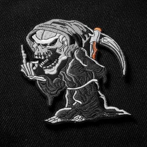 Può includere: Toppa ricamata raffigurante un'immagine della Morte in abito e cappuccio neri, con una falce. La Morte indica con un dito. La toppa presenta un design dettagliato in scala di grigi con accenti arancioni sulla falce.