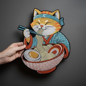 Puede incluir: Parche bordado con un gato de dibujos animados con una diadema azul y un kimono, comiendo fideos ramen con palillos. El cuenco incluye huevos y es rojo y blanco. El gato es naranja, blanco y amarillo.