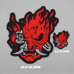 Peut inclure: Deux écussons brodés avec un motif de masque oni rouge et noir. Le plus grand mesure 22,8 x 32,2 cm et le plus petit 8,1 x 9,1 cm. Les écussons ont des accents blancs et noirs.