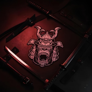Op de afbeelding: Een patch met een gorilla die een samoeraihelm draagt, omringd door verschillende zwarte katana's. De gorilla brult en de katana's zijn rond de patch gerangschikt. De bladen van de katana's reflecteren rood licht, wat een dramatisch effect creëert.