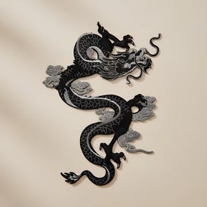 Op de afbeelding: Een zwart en zilver geborduurd drakenpatch met ingewikkelde details. De draak wordt afgebeeld in een dynamische pose, met zijn lichaam gebogen en zijn klauwen uitgestrekt. Het ontwerp bevat zilveren wolken.