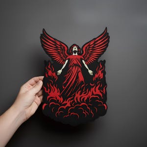 May include: A red and black embroidered patch featuring an angel with outstretched wings and arms, rising from flames. The angel is wearing a flowing red gown. The patch has a black border and is held by a hand.