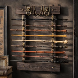 May include: A dark wood wall-mounted display rack featuring two horizontal planks, brass lion head knockers with rings, and a central chain. Eight wands of varying brown, black, and tan tones are held by brass hooks. The bottom plank reads Hogwarts Collection.