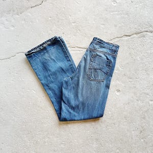 May include: Light blue denim jeans with a classic five-pocket design. The jeans are folded and laid flat, showcasing the faded wash and stitching details. The jeans are made of a durable denim material.