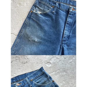 Puede incluir: Primer plano de unos vaqueros de mezclilla azul vintage con detalles desgastados. Los vaqueros presentan un dise&ntilde;o cl&aacute;sico de cinco bolsillos, cierre de bot&oacute;n y cremallera, y desgaste visible en la tela, incluyendo un bolsillo deshilachado y peque&ntilde;os agujeros.