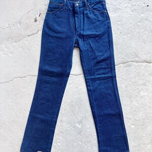 May include: Dark blue denim jeans with a straight leg cut. The jeans feature a button and zip fly, and classic five-pocket design. The denim is a medium weight, suitable for all-season wear. The jeans are laid flat on a light-colored surface.