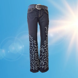 Könnte beinhalten: Dunkelblaue Jeans aus Denim mit einem weißen, geschwungenen Blumenmuster an den unteren Hosenbeinen. Die Jeans ist mit einem schwarzen Ledergürtel mit silberfarbener Metallschnalle ausgestattet. Das Design umfasst Standardtaschen und sichtbare Nähte.