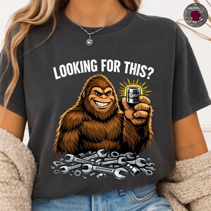 May include: Dark gray t-shirt with the text "LOOKING FOR THIS?" above a cartoon Bigfoot holding a 10mm socket. The Bigfoot is smiling and surrounded by wrenches.