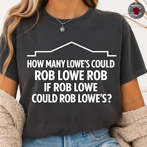 May include: Dark grey t-shirt with white text. The text reads "HOW MANY LOWE'S COULD ROB LOWE ROB IF ROB LOWE COULD ROB LOWE'S?" The text is stacked with a house outline above it.