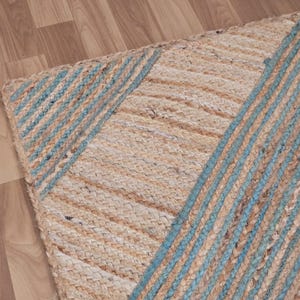 Op de afbeelding: Een rechthoekig jute vloerkleed met een geweven textuur. Het vloerkleed heeft een natuurlijke beige kleur met diagonale lichtblauwe strepen. Het vloerkleed ligt op een houten vloer.