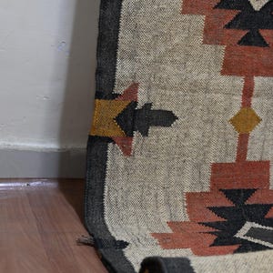 Puede incluir: Una alfombra enrollada con un patr&oacute;n geom&eacute;trico beige, negro y &oacute;xido. El dise&ntilde;o incluye formas repetidas en negro, &oacute;xido y amarillo. La alfombra est&aacute; hecha de material tejido y est&aacute; parcialmente enrollada, mostrando la parte inferior.