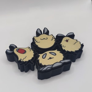 Puede incluir: Un conjunto de imanes con forma de oso panda. Cada imán presenta un contorno negro, una cara de color beige claro y detalles negros. Los imanes están dispuestos sobre una superficie blanca.