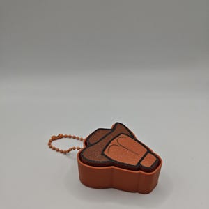 Peut inclure: Un petit r&eacute;cipient orange en forme de chapeau de cowboy avec un bord marron fonc&eacute; et une cha&icirc;nette &agrave; billes orange assortie attach&eacute;e sur le c&ocirc;t&eacute;. L'objet pr&eacute;sente une surface textur&eacute;e et un design moul&eacute; distinct imitant la forme d'un chapeau.
