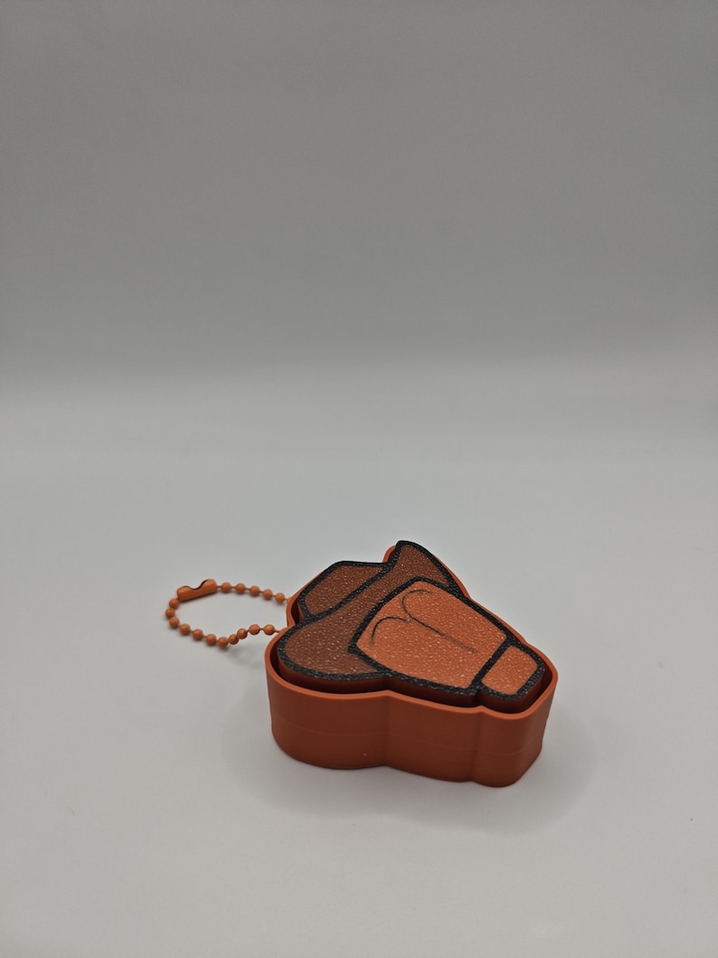 Peut inclure: Un petit r&eacute;cipient orange en forme de chapeau de cowboy avec un bord marron fonc&eacute; et une cha&icirc;nette &agrave; billes orange assortie attach&eacute;e sur le c&ocirc;t&eacute;. L'objet pr&eacute;sente une surface textur&eacute;e et un design moul&eacute; distinct imitant la forme d'un chapeau.