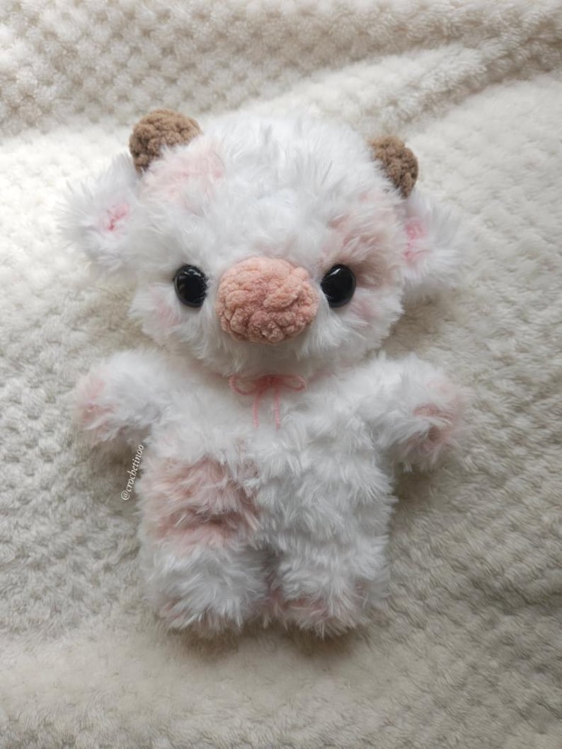 Pu&ograve; includere: Un peluche a forma di mucca fatto a mano, bianco con macchie rosa. Ha grandi occhi neri, un naso rosa e piccole corna marroni. Un piccolo fiocco rosa adorna il collo. Il giocattolo &egrave; realizzato in materiale morbido e soffice.