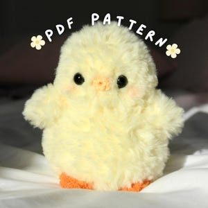 Op de afbeelding: Een zachtgele pluche kuiken met zwarte ogen, een perzikkleurige snavel en oranje voeten. Het kuiken heeft roze wangen en is gemaakt van zacht, pluizig materiaal. De tekst "PDF PATTERN" staat in een boog boven het kuiken, met bloemaccenten.