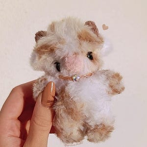 Pu&ograve; includere: Una piccola mucca di peluche con un motivo a macchie bianche e marroni. Il giocattolo ha un naso rosa, occhi neri e piccole orecchie marroni. Indossa un collare rosa con un piccolo ciondolo scintillante. Il giocattolo &egrave; morbido e soffice.