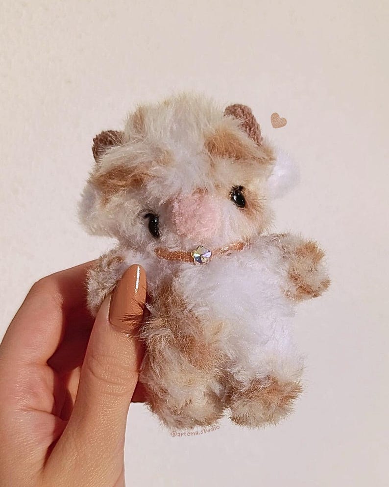 Pu&ograve; includere: Una piccola mucca di peluche con un motivo a macchie bianche e marroni. Il giocattolo ha un naso rosa, occhi neri e piccole orecchie marroni. Indossa un collare rosa con un piccolo ciondolo scintillante. Il giocattolo &egrave; morbido e soffice.